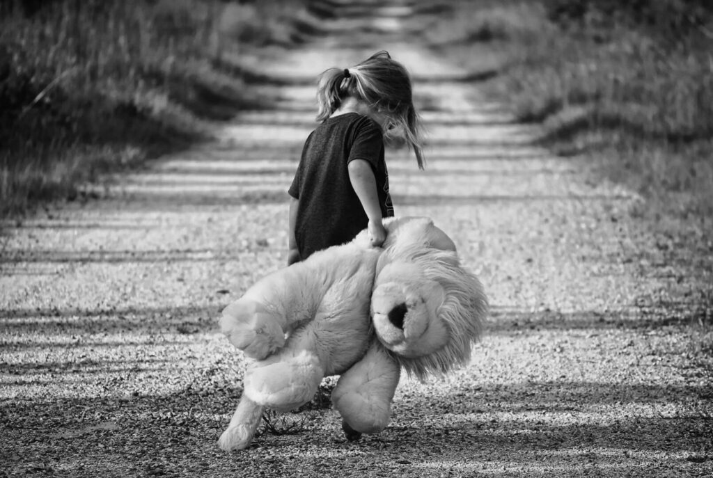 Niña caminando sola por un camino de tierra mientras sostiene un peluche de león.